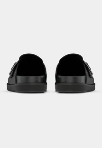 Μαύρα παπούτσια τύπου slip-on με λεία υφή, στρογγυλεμένη πίσω πλευρά και ρυθμιζόμενο λουράκι στο πλάι. Διαθέτουν λάστιχο σόλας με καλή πρόσφυση.