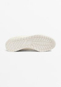 Weiße Sneaker-Sohle mit einer strukturierten Gumm OBERFLÄCHE, die ein Chevron-Profil und ein eingeprägtes Logo aufweist. Der glatte obere Rand verbessert den Grip.