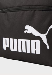 Svart stoffveske med et fremtredende hvitt "PUMA"-logo og en hoppende puma-grafikk; glidelås lukking med teksturert overflate.