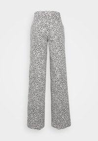 Pantalon taille haute à jambes larges avec un motif de cœur abstrait noir et blanc, vu de dos sur un fond uni clair.