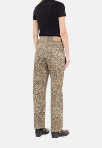 Pantalones de tiro alto con estampado de leopardo, confeccionados con un tejido resistente. Presentan piernas rectas y una etiqueta de cuero marrón en la cinturilla trasera. Se llevan botas negras.