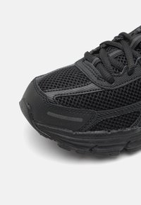 Baskets de sport noires avec tige en maille, accents texturés, bout arrondi et semelle extérieure épaisse en caoutchouc. Les lacets sont également noirs, maintenant un design uniforme.