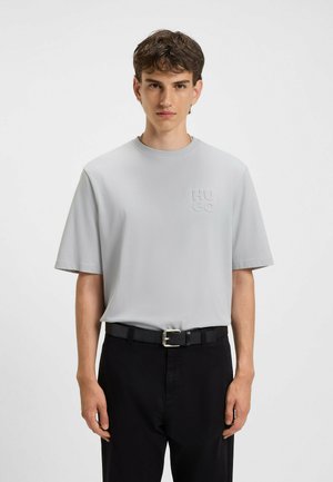Lysegrå kortærmet t-shirt med rund halsudskæring og prægede "HUGO" logo. Båret med sorte bukser og et sort bælte med en sølvspænde.