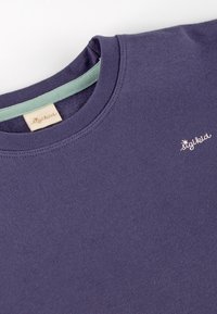 Purple cotton t-shirt featuring a round neckline and a light green accent inside the collar, with a small white embroidered logo.
