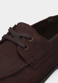 Καφέ σουέντ casual παπούτσι με στρογγυλή μύτη, κλείσιμο με κορδόνια και ραμμένες λεπτομέρειες στο πάνω μέρος.