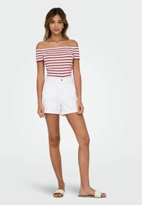 Randig off-shoulder topp i röd och vit, parat med högmidjade vita denimshorts med knappstängning och vända ärmslutar.