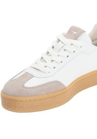 Weißer Sneaker mit beigen Wildledereinsätzen, runder Zehenpartie, flachen Schnürsenkeln und strukturierter Gummisohle. Verfügt über dezente Nähte und eine geprägte Marke.