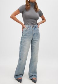 Grå ribbad polotröja matchad med ljusblå högmidjade jeans. Jeans har en avslappnad passform och subtil blekning, med minimal detaljering.