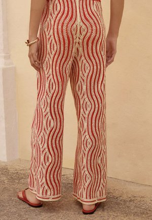 Rode en crèmekleurige gestreepte wijde broek met golvende lijnen, textuurstof en een relaxte pasvorm, gecombineerd met eenvoudige platte sandalen.