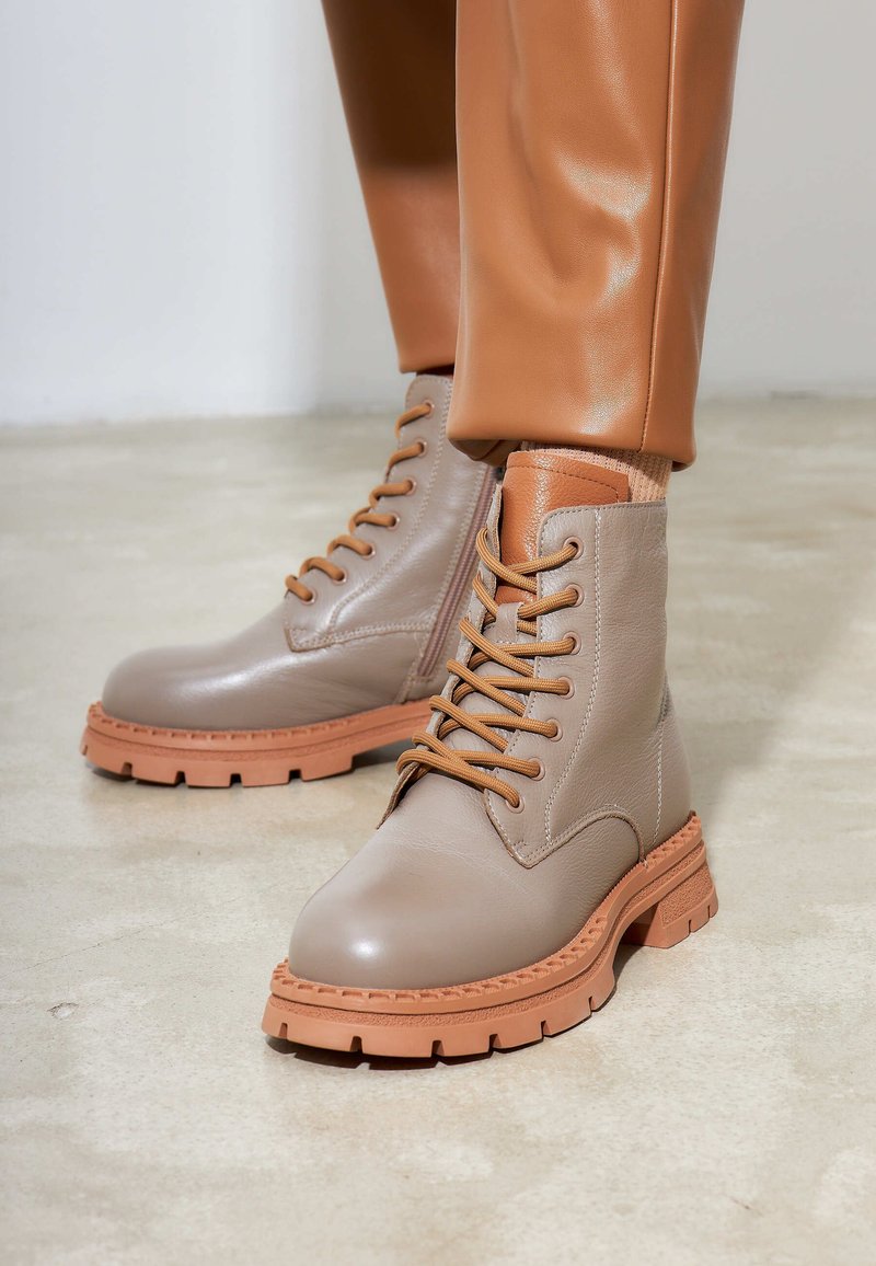 Bottines en cuir beige avec des accents marron, design lacé, languette texturée et semelles en caoutchouc épaisses. Convient à diverses conditions météorologiques.