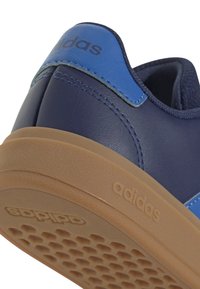 Zapatilla de cuero azul marino con acentos azules, que presenta una suela de goma texturizada y el logotipo de adidas visible en el talón. Acabado suave en general.