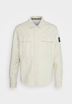 Šviesiai kreminė mygtukinė marškiniai, pagaminti iš medvilnės, su dviem krūtinės kišenėmis, smailiu apykakle ir logotipo žyme kairiajame rankove.