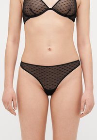 Svart genomskinlig lingerie-set med prickigt mönster, triangelbehå och minimal täckande string, med en delikat kant och mjuk textur.
