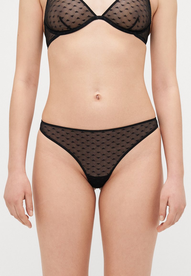 Svart genomskinlig lingerie-set med prickigt mönster, triangelbehå och minimal täckande string, med en delikat kant och mjuk textur.