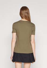 Camiseta de algodón verde oliva de manga corta, con cuello redondo y una textura suave, vista desde la espalda con una falda negra visible.