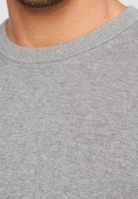 Grauer Strickpullover mit rundem Halsausschnitt, versehen mit einem dezenten "Esprit"-Logo in passendem Grau auf der Vorderseite. Weiche Textur, lässiges Design.
