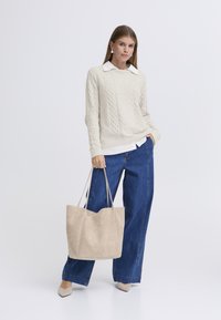 Maglione beige chiaro lavorato a maglia con motivo a trecce, camicia bianca con colletto sotto, jeans blu larghi, borsa tote color taupe e décolleté beige.