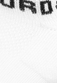 Calcetín blanco con texto negro tejido. El material es texturizado, con un tejido fino y un puño elástico para mayor comodidad y ajuste.