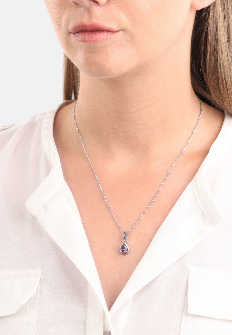 Silverhalsband med ett tvinnat kedja och en päronformad lila ädelsten som hängs över en vit blus.