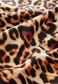 Tkanina s leopardím vzorem, která obsahuje černé skvrny a oranžovo-hnědé akcenty na krémovém pozadí, s měkkým a strukturovaným vzhledem.