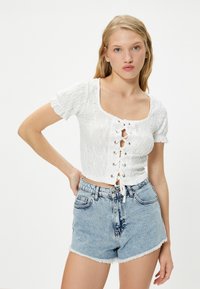Witte eyelet crop top met een vierkante halslijn en een vetersluiting aan de voorkant, gecombineerd met lichtblauwe denim shorts met hoge taille en een rafelige zoom.