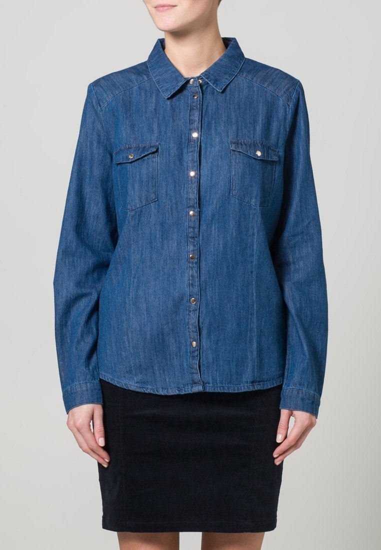 Camicia in denim blu scuro, con colletto, chiusura frontale con bottoni, due tasche sul petto e maniche lunghe. Tessuto liscio e vestibilità standard.