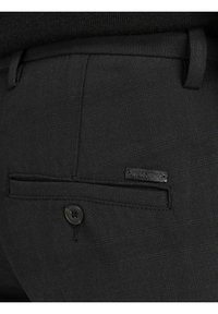 Black trousers with a textured fabric, featuring a back pocket with a button closure and a small label that reads "Jack & Jones."