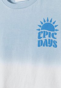 Gaiši zils kokvilnas T-krekls ar gradienta dizainu, uz kura priekšpuses izvietots uzraksts "EPIC DAYS" un saules grafika tumšāk zblue tintē.