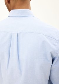 Lichtblauw katoenen shirt met een klassieke kraag, rugplooien en subtiele textuur, gezien van de achterkant.