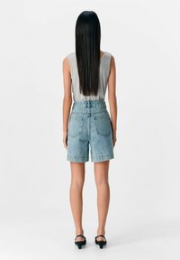 Shorts di jeans azzurri a vita alta con orli risvoltati, dotati di due tasche posteriori. Abbinati a un top grigio senza maniche.