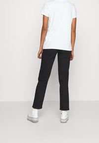 Vit bomullströja med korta ärmar, ihop med svarta raka byxor och vita sneakers med svarta ränder på sulan.