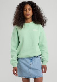 Helles mintgrünes Sweatshirt mit Rundhalsausschnitt, lockerer Passform und gerippten Bündchen, kombiniert mit einem hellblauen Jeansrock.