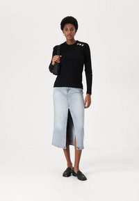 Sort ribbet langærmet top med guld hjerteaksenter, parret med en lys blå denimnederdel med frontslids, båret med sorte slip-on sko.