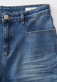 Jeans denim di un blu medio con vestibilità regolare, caratterizzati da un bottone argento, tasche anteriori e un leggero effetto sbiadito sulle cosce.