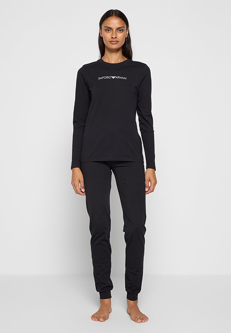Top noir à manches longues et pantalon ajusté en tissu doux, avec le logo "Emporio Armani" en blanc sur la poitrine.