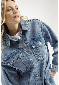 Jasnobłękitna kurtka dżinsowa o klasycznym fasonie, z dwiema kieszeniami z przodu, zapięciem na guziki i lekko przetartą strukturą.