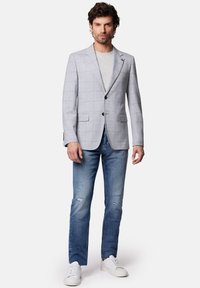 Jasnoszary blazer w kratę z klapami, zestawiony z szarym t-shirtem i zniszczonymi niebieskimi dżinsami. Białe sneakersy dopełniają całość.