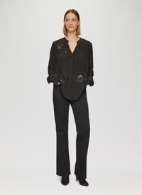 Zwarte blouse met V-hals, voorzien van bewerkte bloemenversieringen op de mouwen en voorkant. Gecombineerd met zwarte aansluitende broeken en enkellaarsjes.