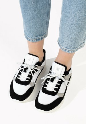 Sorte og hvide sneakers med tekstureret stof, der har et grå accentpanel, hvide snørebånd og et logo på tungen.