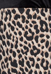 Luipaardprint stof met zwarte vlekken op een beige achtergrond, met een gladde textuur en een contrasterend zwart deel aan de bovenkant.