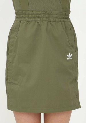 Oliivinvihreä Adidas-hame, jossa joustava vyötärönauha, sivussa painonapit, sivutaskut ja valkoinen Adidas-trefoil-logo oikealla etupuolella.