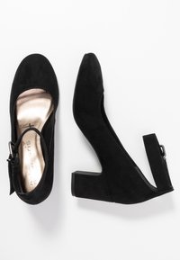 Scarpe con tacco in suede nero, con punta chiusa, cinturino alla caviglia e tacco basso a blocco. L'interno presenta un rivestimento dorato metallizzato.