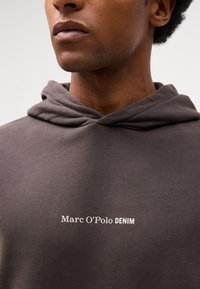 Donkergrijze hoodie van zachte stof, met een trekkoordcapuchon en een wit "Marc O’Polo DENIM" logo op de borst.