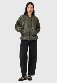 Quilted olivengrøn bomberjakke med frontlukning i snap, elastisk talje og ribstrikkede manchetter, parret med sorte vidde bukser og sorte sko.