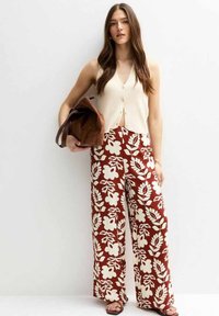 Haut sans manches crème avec des boutons, associé à un pantalon large marron à motifs floraux. L'ensemble présente des motifs floraux de couleur claire sur un fond chocolat.