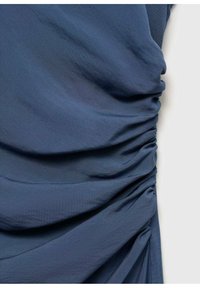 Gros plan sur un tissu bleu avec une texture froncée formant des plis et des ombres le long de sa longueur sur un fond clair.