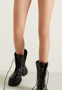 Czarne lakierowane botki bojowe z grubą podeszwą, sznurowane, w połączeniu z jasnymi zakolanówkami z siateczki z wzorem w romby.