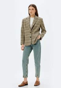 Rutigt kavaj i bruna och beige nyanser, matchat med ljusblå högmidjade jeans och bruna loafers; har en skräddarsydd passform och fickor.