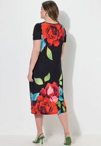 Czarna sukienka w kwiaty z dużymi czerwonymi i różowymi różami oraz zielonymi liśćmi. Krótkie rękawy i długość do kolan. Zestawiona z zielonymi szpilkami.