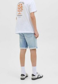 Shorts di denim azzurro chiaro con risvolti, abbinati a una t-shirt bianca con grafica che presenta un design di palme e testo arancione. Inclusi calzature casual.
